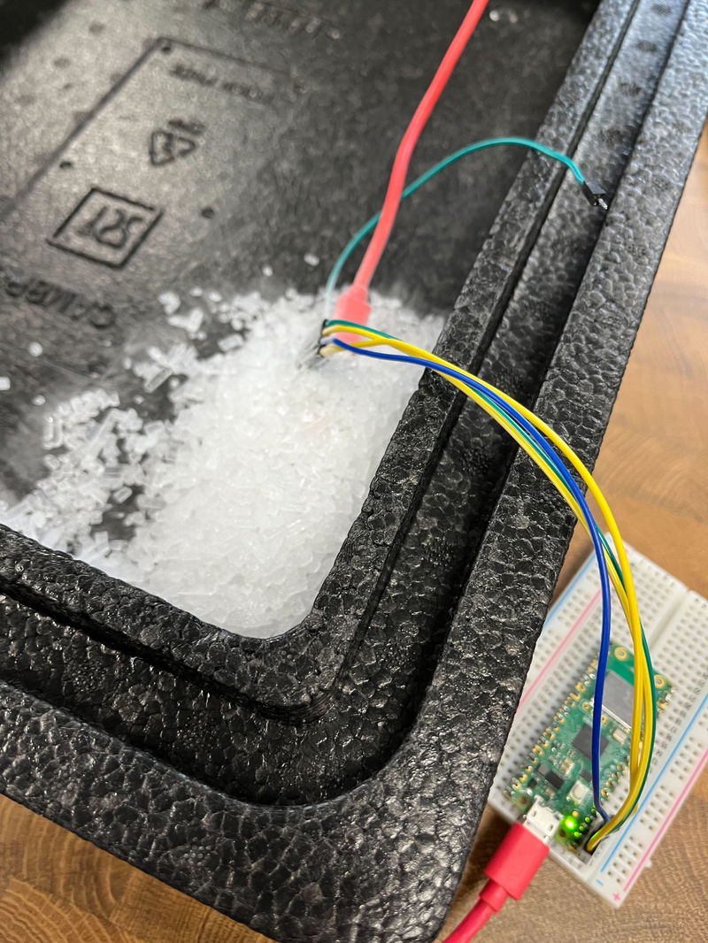 A pile of dry ice covering a Pico 2, with various wires coming out, some connected to a Pico W sitting outside of the box